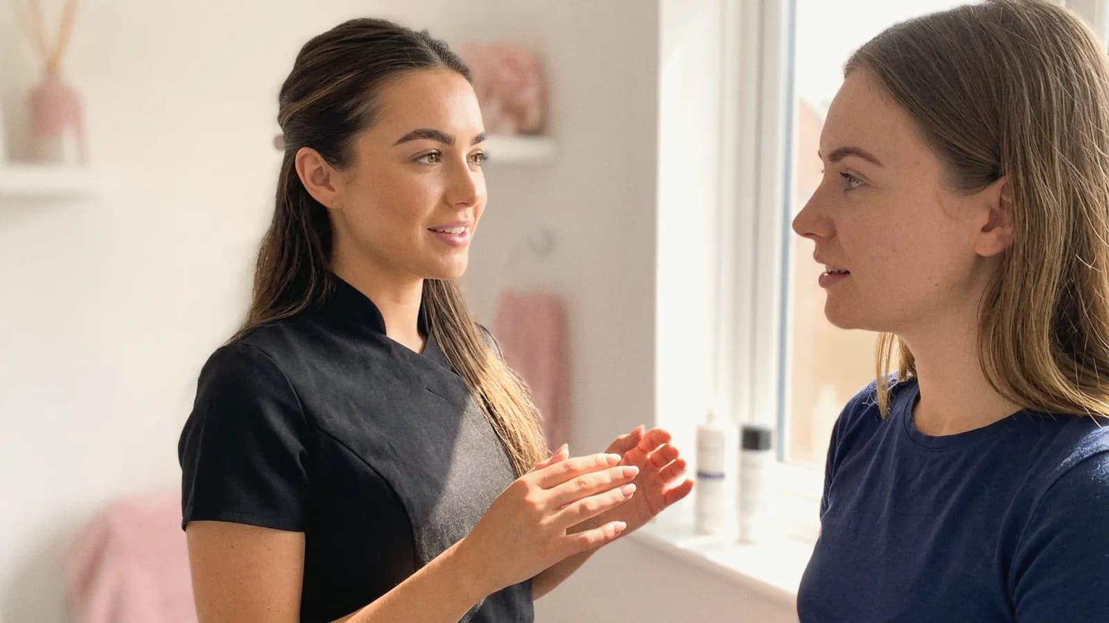 A practitioner explains a plan to a client beside a bright clinic window.